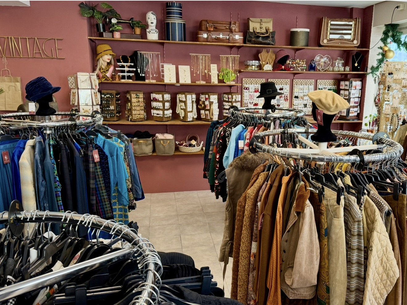 Interieur van VintageGlitch met rekken vintage kleding, hoeden en een wand met sieraden tegen oudroze muren