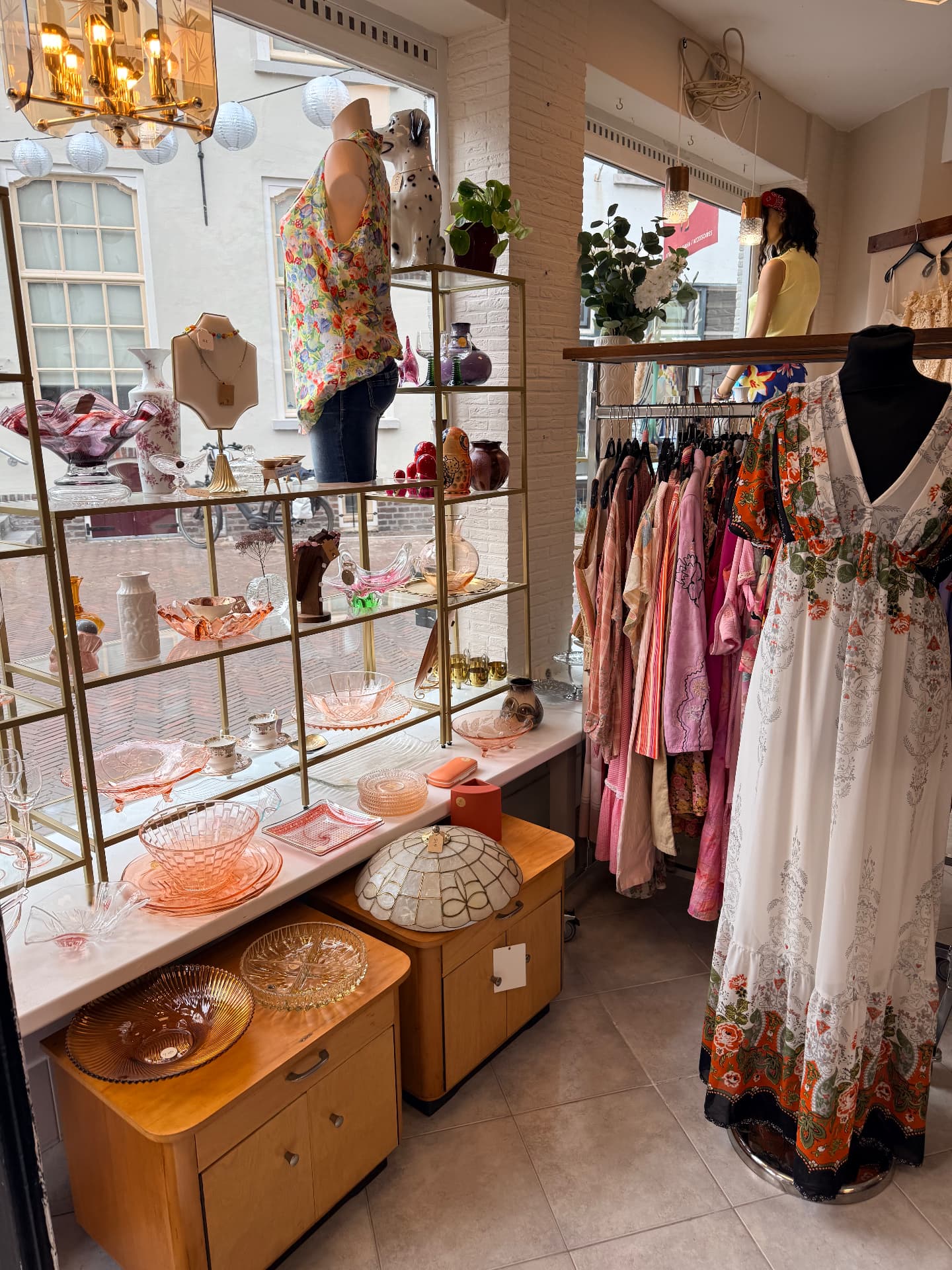 Vintage jurken in roze en oranje tinten naast een etalage met roze perssglas en kristal
