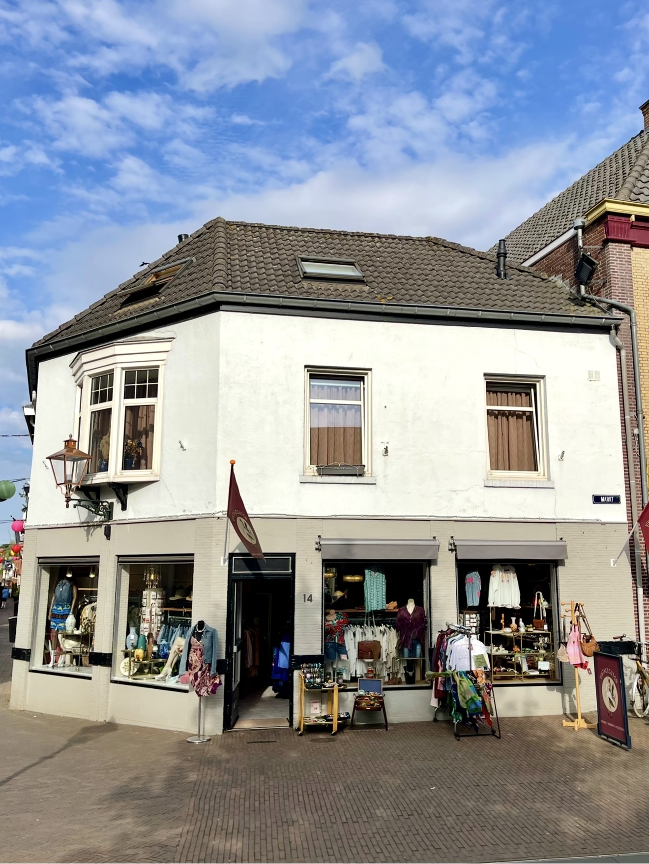 Het hoekpand van VintageGlitch aan Markt 14 in Gennep met etalages vol vintage kleding en een bordeauxrode vlag